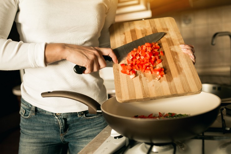 Una persona versa in una padella da un tagliere dei pomodori tagliati a pezzetti