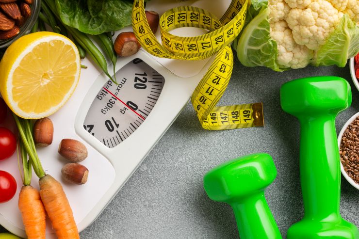 Una bilancia accanto ad alimenti sani, pesetti da palestra e un metro