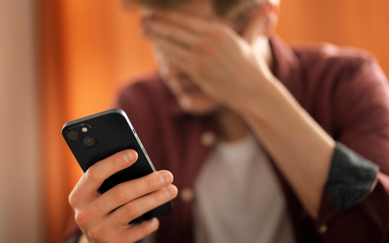 Una persona esasperata tiene una mano sulla testa mentre l'altra regge uno smartphone