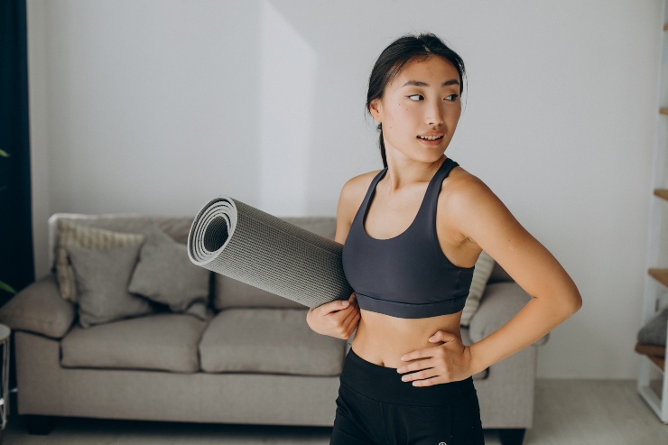 Una ragazza in salotto con in mano un tappetino fitness