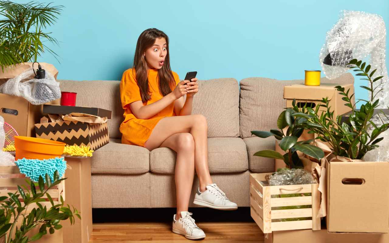 Una donna sorpresa mentre guarda lo schermo dello smartphone seduta sul divano