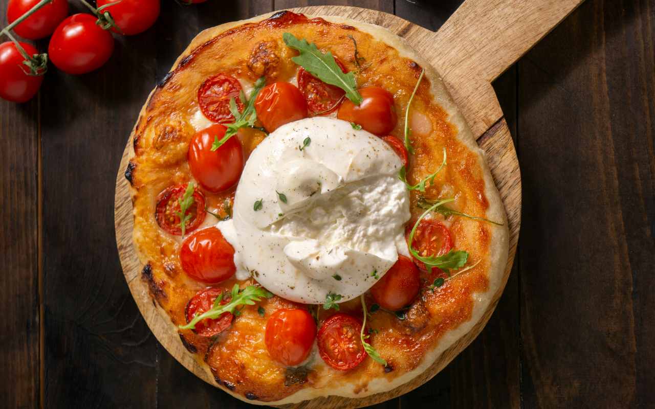 Una pizza margherita con burrata su un tagliere di legno