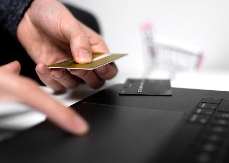 Una persona fa una ricerca al pc mentre tiene una carta di pagamento in mano