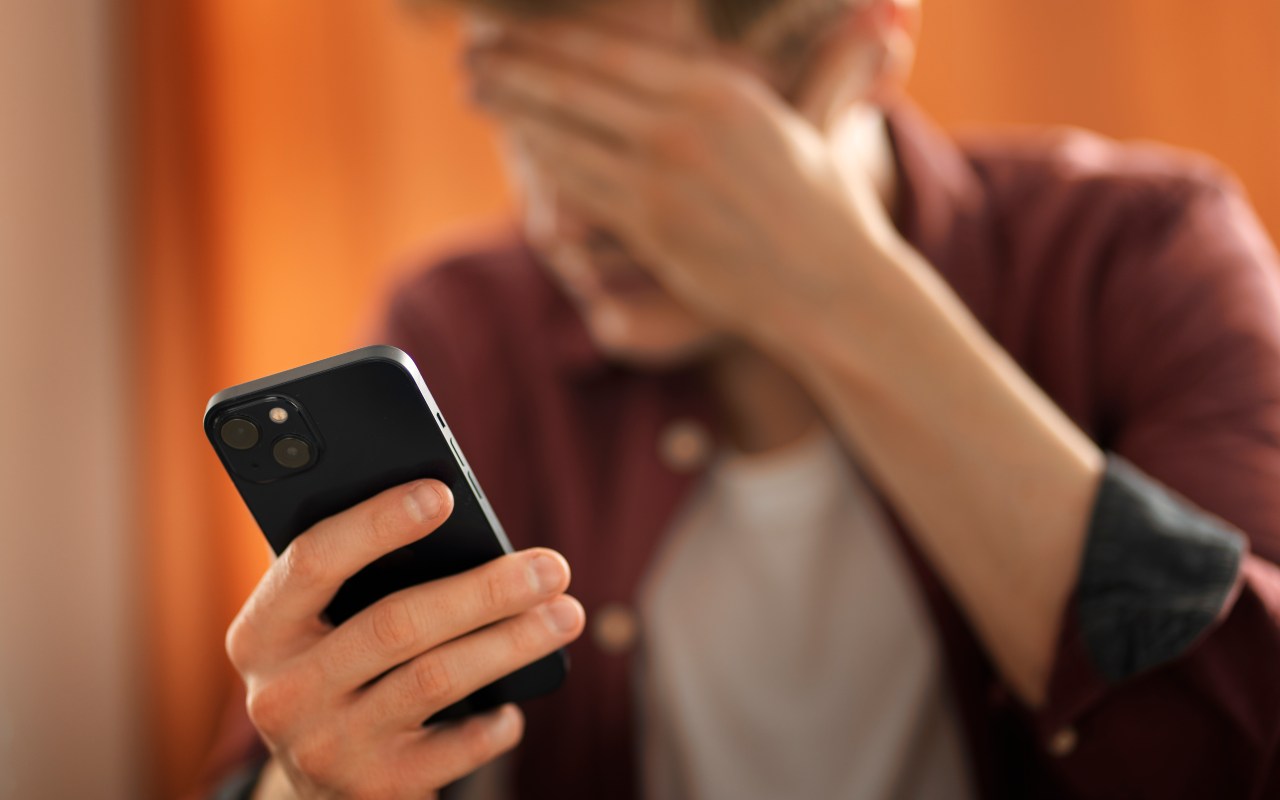 Un uomo tiene una mano sul viso e il telefono nell'altra