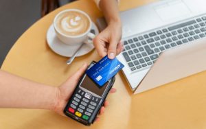 Una persona seduta al tavolino con cappuccino e computer mentre paga con la carta di credito