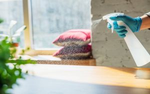 Una persona pulisce un tavolo di legno con un detergente in spray