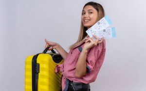 Una ragazza tiene in mano due biglietti aerei e una valigia da imbarco