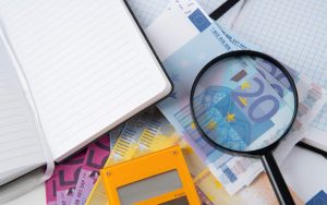 Lente di ingrandimento su banconote da 20 euro accanto a un blocco per gli appunti e calcolatrice