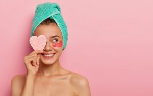 Una ragazza tiene in mano una spugna a forma di cuore indossando dei patch eye