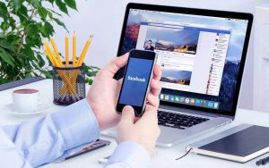Una persona seduta alla scrivania utilizza lo smartphone per accedere a Facebook