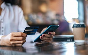 Una persona seduta a un tavolo tiene in mano una carta prepagata e uno smartphone