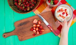 Preparazione di un dolce con fragole tagliate a fettine e panna